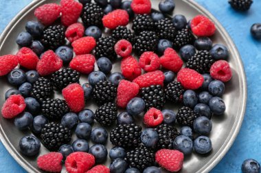 Mavi arkaplanda farklı taze böğürtlen tabağı, yakın plan.