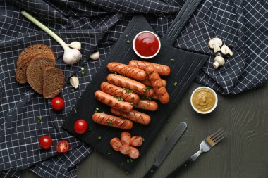 Lezzetli ızgara sosis ve siyah ahşap masada sebzeler.