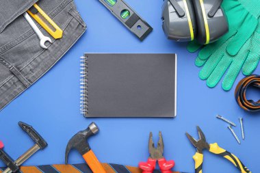 Not defteri, farklı aletler ve koruyucu ekipmanlar mavi arka planda. İşçi Bayramı kutlamaları