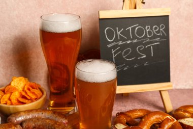 Soğuk bira bardakları, kelime karatahta OKTOBERFEST ve pembe arka planda farklı atıştırmalıklar