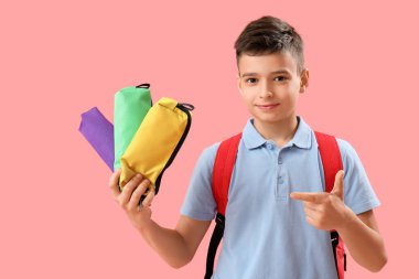 Küçük okul çocuğu pembe arka plandaki kalem kutularını işaret ediyor.