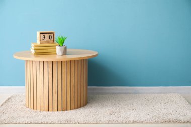 Kitaplı kahve masası, küp takvimi ve mavi duvarın yanındaki bitki örtüsü.