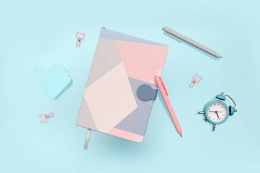 Mavi arkaplanda farklı kırtasiye ve alarm saatine sahip defterler