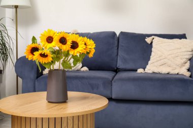 Oturma odasındaki ahşap sehpanın üzerinde güzel ayçiçekleri olan mavi kanepe ve vazo