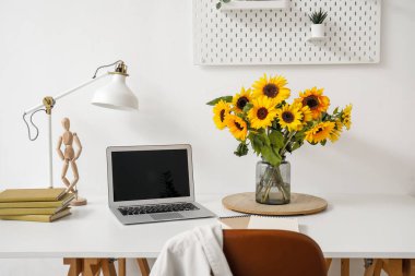 Güzel ayçiçekli vazo ve beyaz masadaki modern laptop, yakın plan.