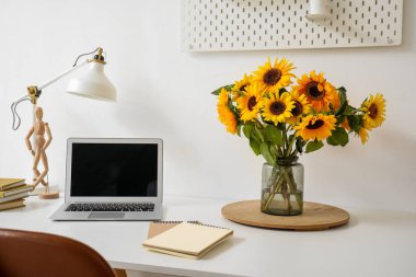 Güzel ayçiçekli vazo ve beyaz masadaki modern laptop, yakın plan.