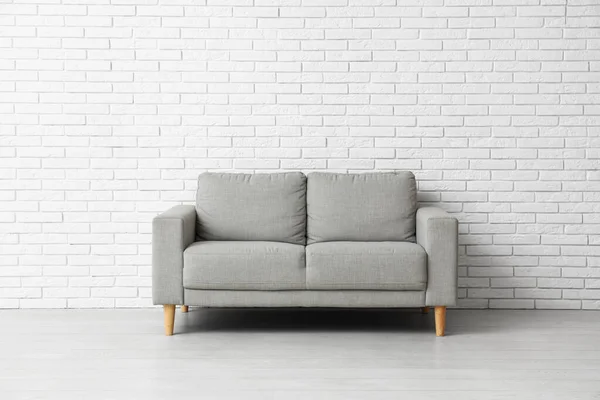 白いレンガの壁の近くの居心地の良い灰色のソファ — ストック写真