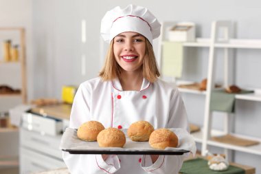 Female baker with tray of tasty buns in kitchen