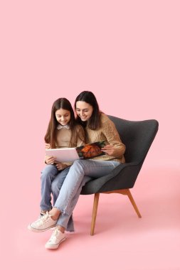 Küçük kız ve annesi pembe arka planda kitap okuyorlar.