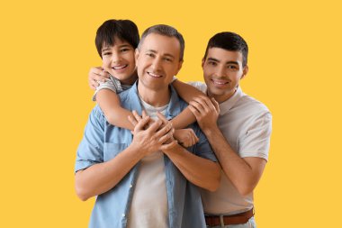 Mutlu küçük çocuk, babası ve büyükbabasıyla sarı arka planda sarılıyor.