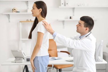 Erkek doktor klinikteki genç kadının duruşunu kontrol ediyor.