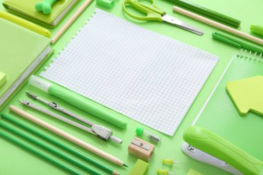 Yeşil zemin üzerinde farklı kırtasiye malzemesi olan boş bir defter