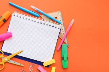 Turuncu zemin üzerinde farklı kırtasiye malzemesi olan boş bir defter