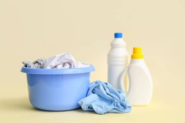 Kirli çamaşırlı plastik leğen ve bej arka planda bir şişe çamaşır deterjanı.
