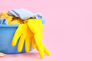 Kirli elbiseli plastik leğen ve pembe arka planda sarı lastik eldiven.