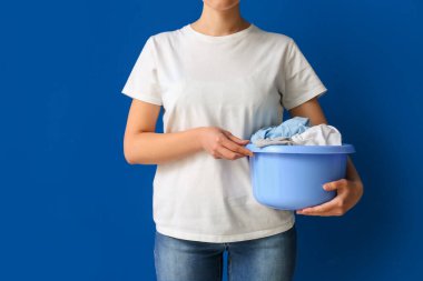 Mavi arka planda kirli çamaşırları olan plastik bir leğen tutan kadın.