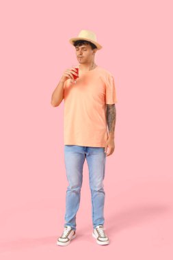 Genç adam pembe arka planda kırmızı meyve suyu içiyor.