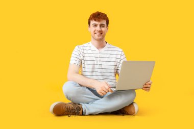 Erkek programcı sarı arka planda dizüstü bilgisayarla çalışıyor