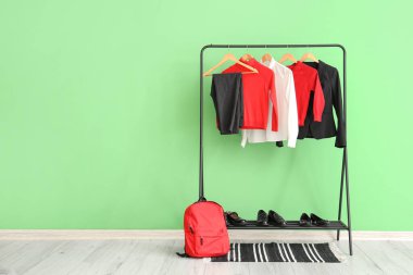 Askıda asılı şık okul üniforması, sırt çantası ve ayakkabılar yeşil duvarın yanında