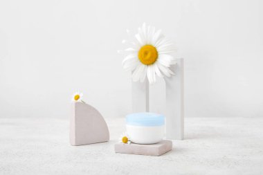 Hafif arkaplanda kozmetik ürün kavanozu, sıva podyumları ve papatya çiçekleri kompozisyonu