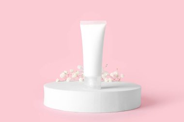 Plaster podyum, kozmetik ürünler tübü ve pembe arka planda alçı çiçekleri.