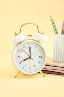 Sarı zemin üzerinde not defterleri ve kırtasiye tutacağı olan alarm saati