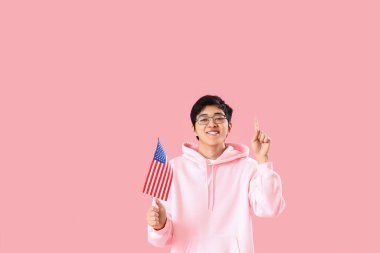 ABD bayraklı genç Asyalı adam pembe arka planda bir şeye bakıyor.