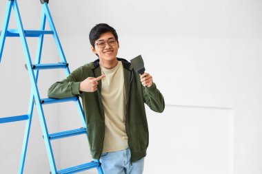 Genç Asyalı adam odada oyuncak bıçağını işaret ediyor.