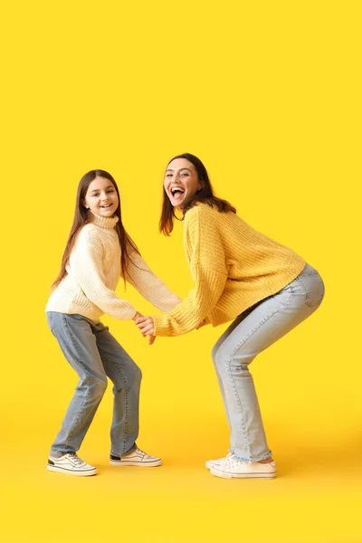 穿着针织毛衣的小女孩和她的母亲在黄色背景下跳舞 — 图库照片