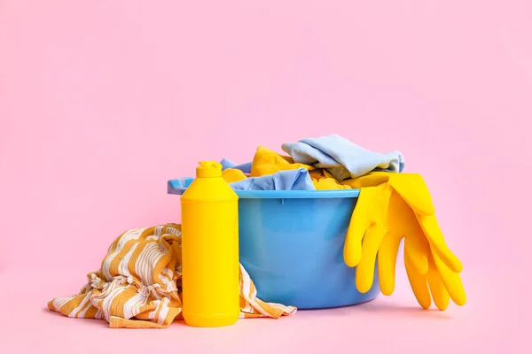 带有脏衣服的塑料盆 一瓶洗衣粉和粉色背景的黄色橡胶手套 — 图库照片