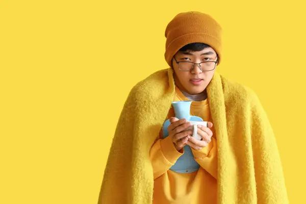 黄色の背景にお茶とお湯のボトルのカップと病気アジアの男 — ストック写真