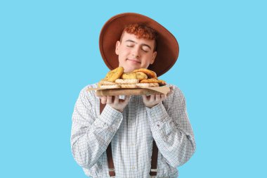 Geleneksel Alman kıyafetleri içinde mavi arka planda atıştırmalıkları olan genç bir adam.