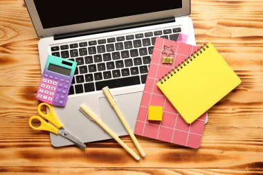 Hesap makineli dizüstü bilgisayar ve kahverengi ahşap arka planda farklı kırtasiye.