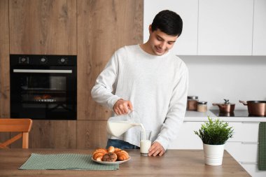 Genç adam mutfakta bardağa süt döküyor.