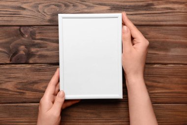 Ahşap arka planda boş fotoğraf çerçevesi tutan kadın.