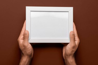 Kahverengi arkaplanda boş fotoğraf çerçevesi tutan adam