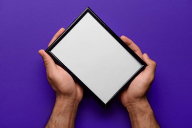 Mor arkaplanda boş fotoğraf çerçevesi tutan adam