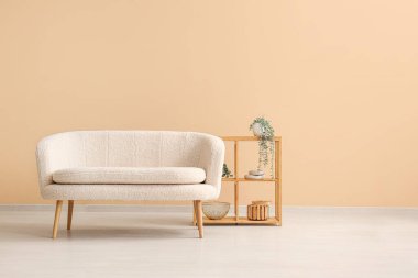 Saf beyaz kanepe ve bej duvarın yanında bitkiler olan raf ünitesi.