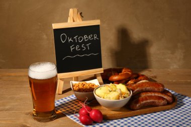 Bir bardak soğuk bira, kelime karatahta OKTOBERFEST ve ahşap arka planda farklı atıştırmalıklar