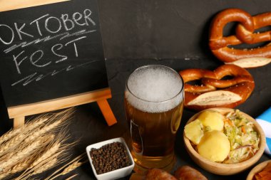 Bir bardak soğuk bira, kelime karatahta OKTOBERFEST ve siyah arka planda farklı atıştırmalıklar.