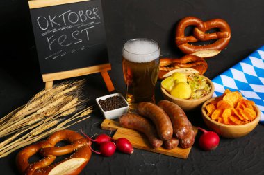 Bir bardak soğuk bira, kelime karatahta OKTOBERFEST ve siyah arka planda farklı atıştırmalıklar.