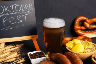 Bir bardak soğuk bira, kelime karatahta OKTOBERFEST ve siyah arka planda farklı atıştırmalıklar.