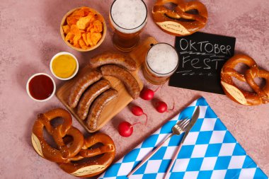 Soğuk bira bardakları, kelime karatahta OKTOBERFEST ve pembe arka planda farklı atıştırmalıklar