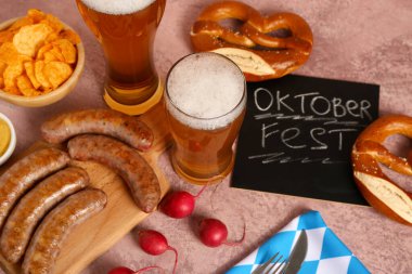 Glasses of cold beer, chalkboard with word OKTOBERFEST and different snacks on pink background clipart