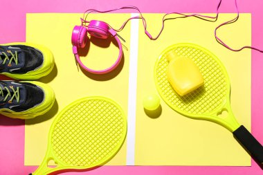 Renkli arka planda güneş kremi, kulaklık ve spor malzemesi içeren kompozisyon