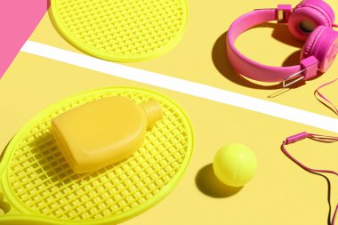 Güneş kremi, kulaklık, tenis raketi ve renkli fonda top ile kompozisyon