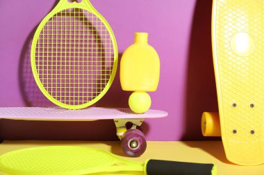 Güneş kremi, kaykay, tenis raketi ve renkli arka planda top içeren kompozisyon