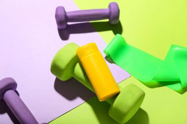Renk arka planında güneş kremi, halterler ve elastik bant ile kompozisyon