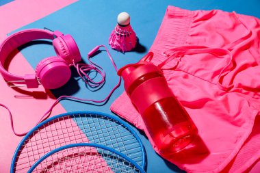 Bir şişe su, kulaklık, badminton raketleri ve renk arkaplanlı mekik sikli kompozisyon