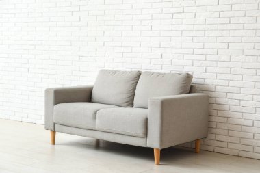 Beyaz tuğla duvarın yanındaki rahat gri kanepe